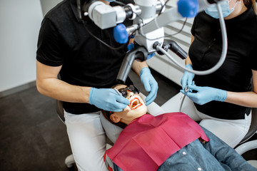 Dentists making dental examination to a young woman with professional microscope