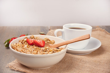 A plate with muesli with strawberries and cuo of tea or coffee on the wooden table