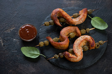 Wooden skewers with bbq pork loin and olives on a stone slate tray, dark brown stone background, horizontal shot