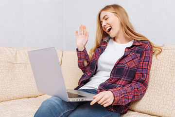 Beautiful girl sitting on the sofa at home, with a laptop, communicating with loved ones on Skype,...