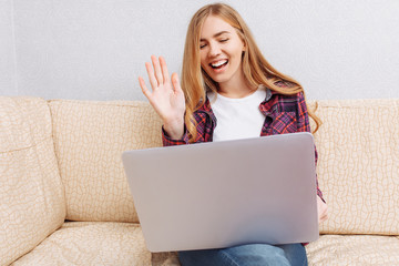Beautiful girl sitting on the sofa at home, with a laptop, communicating with loved ones on Skype,...
