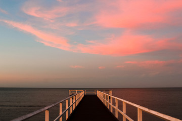Obraz premium Wooden pier during sunset overseeing the ocean with pink horizon and turquoise sky (Hervey Bay near Fraser Island, Queensland, Australia)