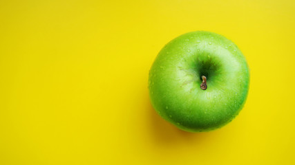 Green apple in water drops on yellow background isolated close up macro top view