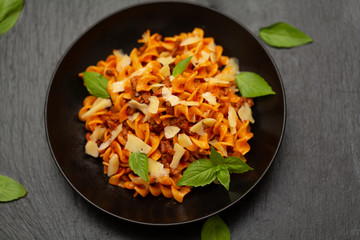 Tasty appetizing classic Italian Fusilli pasta with tomato sauce, cheese parmesan, beef and basil in black bowl on table. View from above.