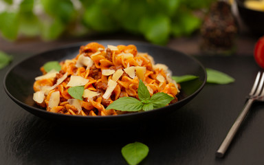 Tasty appetizing classic Italian Fusilli pasta with tomato sauce, cheese Parmesan, beef and basil in black bowl on table. 