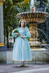Fototapeta premium Girl with a bouquet in vintage dress standing by fountain