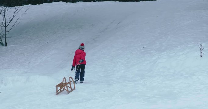 WIDE Cute little kid boy child dragging sledge to the top of the hill. Child plays outdoors in snow, winter fun. 4K UHD 60 FPS SLOW MOTION