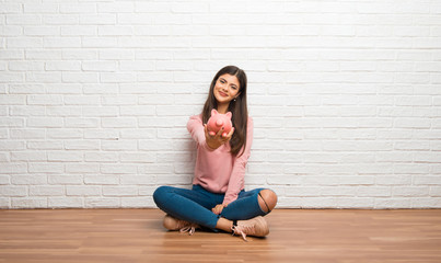 Fototapeta na wymiar Teenager girl sitting on the floor in a room holding a piggybank