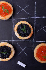 Red and black caviar in tartlets on a chalkboard with tic tac toe game
