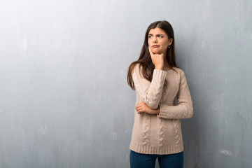 Teenager girl with sweater on a vintage wall having doubts while looking up