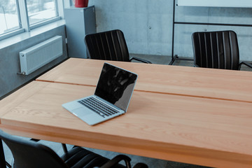 Large bright office in a loft style, with windows, concrete walls and a laptop on a wooden table