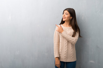 Teenager girl with sweater on a vintage wall pointing to the side to present a product