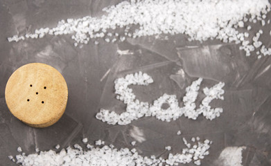 Spilled sea salt on a stone table top. The salt lies on the table with the inscription SALT. Grey backgraund