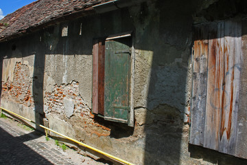 One level, old abandoned house with fallen plaster and obsolete wooden painted shutters.