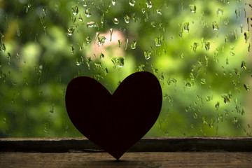 Silhouette of heart on an old wooden window and rain drops background