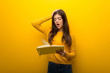 Teenager girl on vibrant yellow background surprised while enjoying reading a book