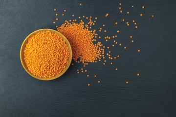 Red lentils in wooden plate on black stone table background