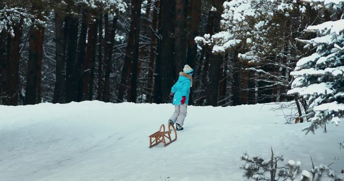 WIDE Cute little kid girl child dragging sledge to the top of the hill. Child plays outdoors in snow, winter fun. 4K UHD 60 FPS SLOW MOTION