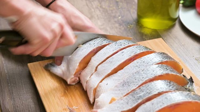 Close-up of female hands are cutting with a knife a large salmon on a wooden table of home cooking