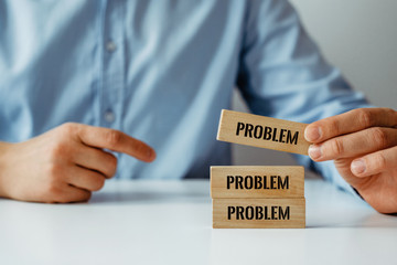 Businessman in a blue shirt arranges wooden jigsaw blocks with the word PROBLEMS. The concept of solving problems, adding or removing problems. Troubleshooting.