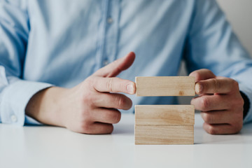 Businessman in a blue shirt arranges wooden jigsaw blocks. The man arranges empty blocks one on top of the other. Different concepts to supplement with content. Business concept, HR.