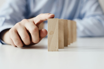 Businessman hand Stopping Falling wooden Dominoes for business solution effect from continuous toppled or risk, strategy and successful intervention. Concept of prosperity in business.