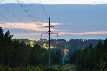 Power lines on a background of green forest, hills, and lights