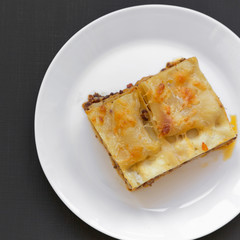 Traditional beef lasagne on a white round plate over black background, top view. Flat lay, from above. Closeup.