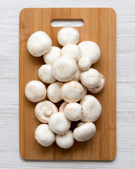 Champignon mushrooms on bamboo board on a white wooden background, top view. From above. Close-up.