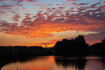 Altocumulus clouds over a lake are beautifully colored by the orange and purple light of the setting sun.  Tranquil scene on an evening in spring, close to the city of Gouda, Holland.