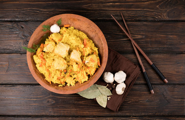 Pilaf with vegetables and chicken in a wooden bowl on a wooden background