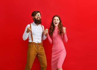 young happy couple won emotionally celebrating win on colored red background.