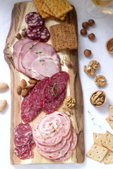 Appetizer of various types of sausages, meats, cheeses and crackers on a wooden board, served to wine.