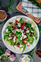 Dish with Arugula on a white plate. Green, fresh arugula on a plate, with white cheese and pasta on a stone countertop. The concept of preparing a fresh and healthy salad. Caring for health.