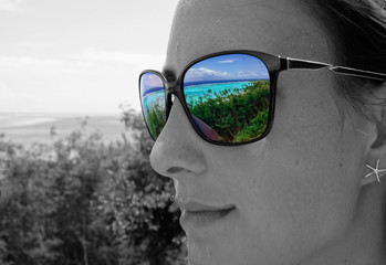 CLOSE UP: Tropical beach and turquoise ocean reflected in woman's sunglasses.
