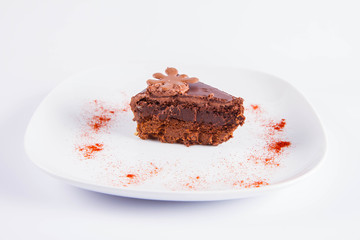 Chocolate cake - a slice on a plate decorated with powdered chili pepper on a white background