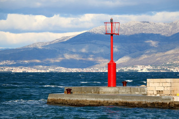 Small red lighthouse on the pier in Sutivan, island Brac, Croatia. Windy and cloudy weather, beautiful landscape.