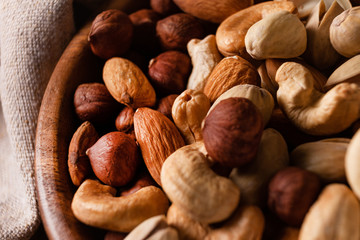 Assortment of nuts in wooden bowl on dark wooden table. Cashew, hazelnuts, almonds and pistachios.