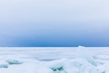 Fototapeta na wymiar The winter gulf of the sea covered with snow and ice. White and blue beautiful landscape with cloudy sky, white surface of the sea and the heap of floes on the shore