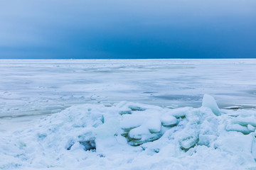 The winter gulf of the sea covered with snow and ice. White and blue beautiful landscape with cloudy sky, white surface of the sea and the heap of floes on the shore
