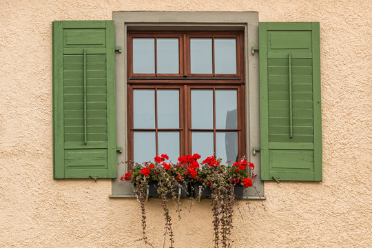 Window with green shutters and a flower box with red flowers