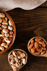 Assortment of nuts in wooden bowl on dark wooden table. Cashew, hazelnuts, almonds and pistachios.