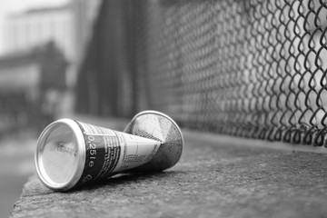 Zerdrückte Dose in schwarz weiß mit Zaun im Hintergrund 