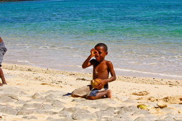 Poor malagasy boy breaking coconuts on the beach