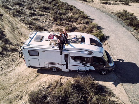 Couple sitting at camper car roof and waving hands