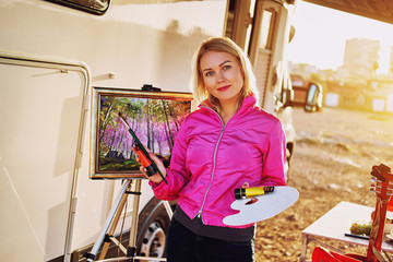Pretty painter woman holds paint brush standing near caravan