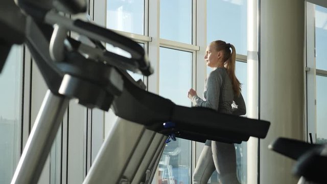 Attractive woman of middle age is running on tread mill in sport gym