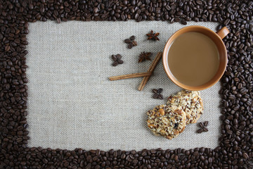 Kawa, ciastka i laski cynamonu na tkaninie z juty, wokół obramowanie z ziaren kawy