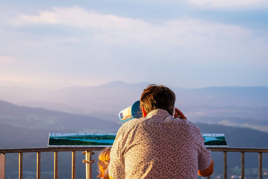The man from the observation tower  in Coin-operated binoculars looks at the mountains. View from back.