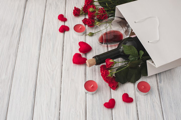 Valentines day. Holiday gift set for lovers. Wine with roses on a white wooden table. Candles and hearts for a romantic event.